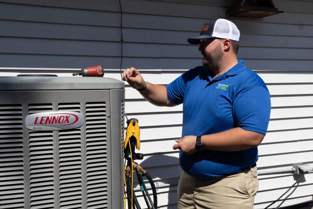 Southern Air technician in blue polo shirt inspects a Lennox Elite air conditioning unit mounted on exterior wall.