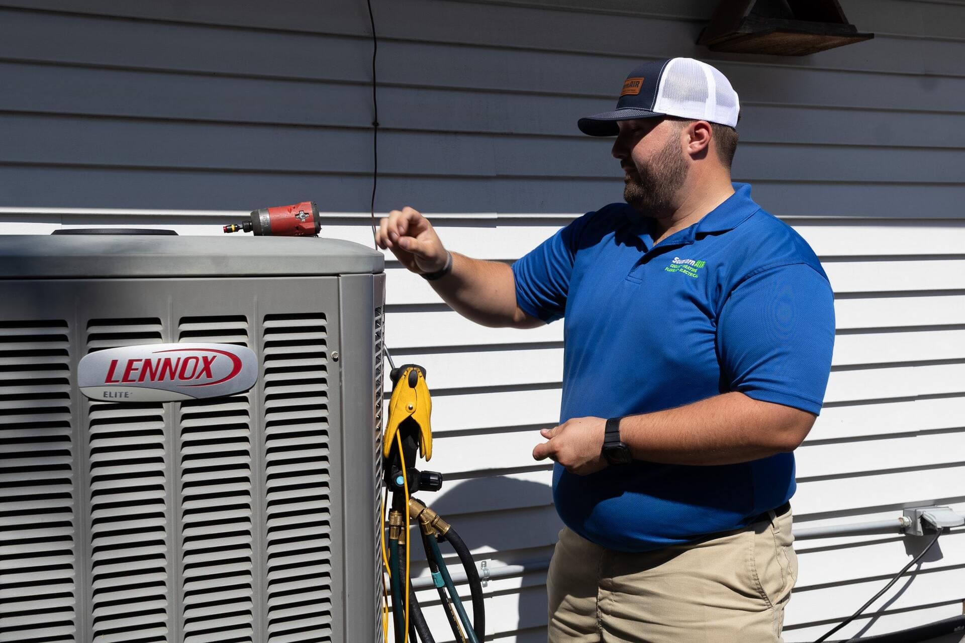Southern Air technician in blue polo shirt inspects a Lennox Elite air conditioning unit mounted on exterior wall.