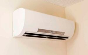 White ductless split AC indoor unit mounted on beige wall with control panel and black air vent.