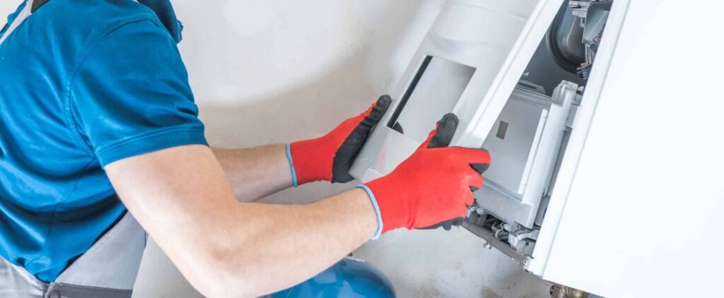 Technician in blue shirt and red gloves installing a residential heating unit during maintenance service.