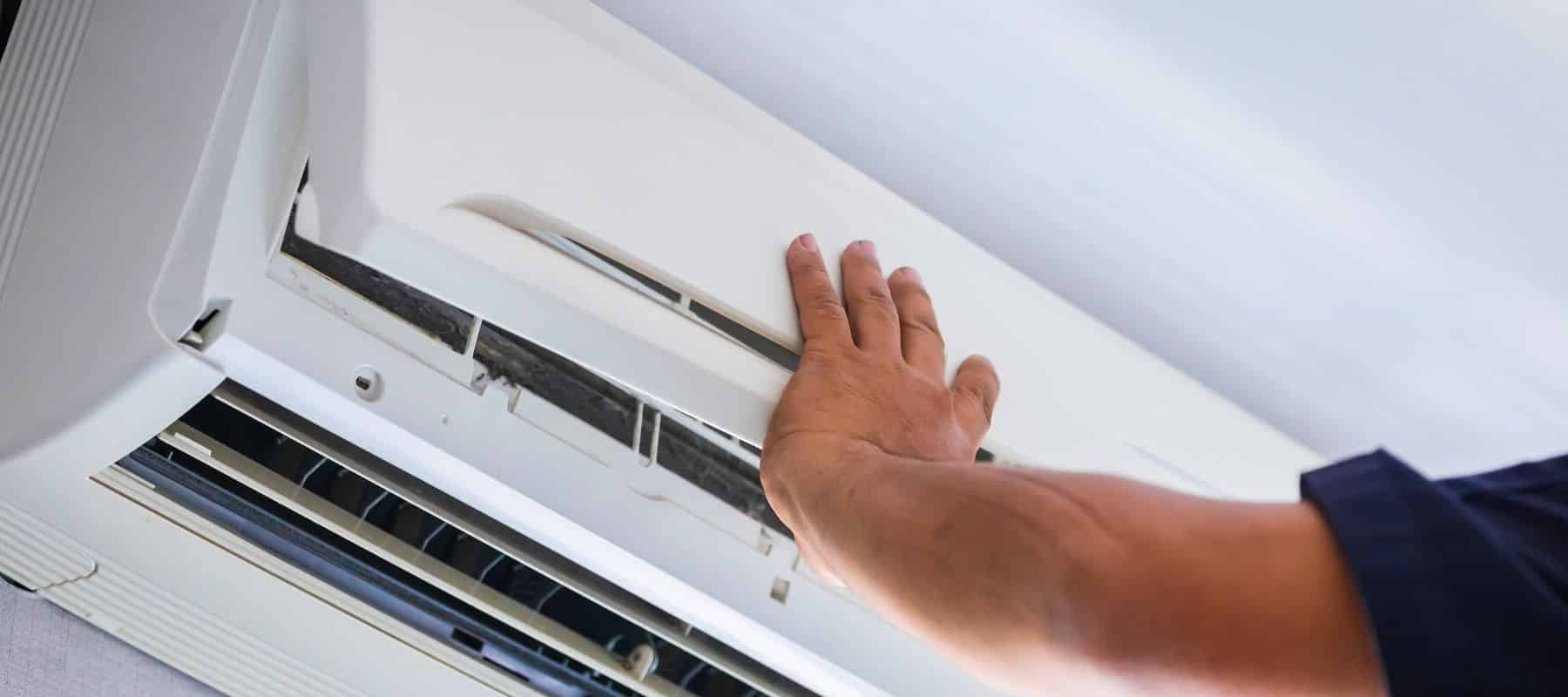 Technician's hand reaching toward an indoor air conditioning unit to perform maintenance or inspection work.